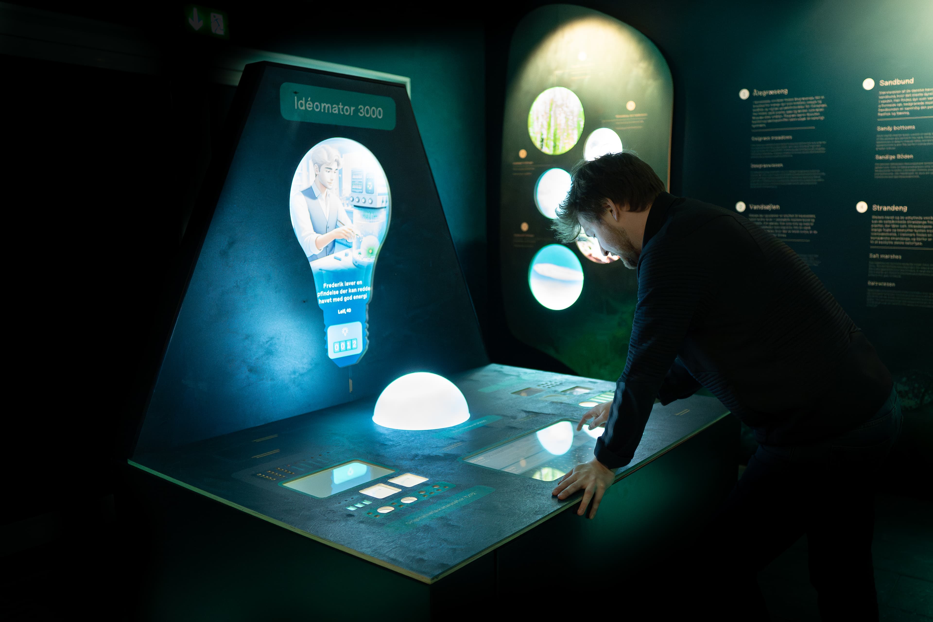 Photo of the Idea Machine enclosure in the Dødvande exhibition at Kattegatcentret, showing the four-display setup and DMX lighting